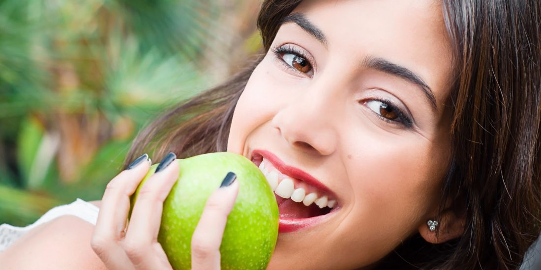 Lachende Frau beißt in einen Apfel