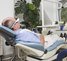 Männlicher Patient mit Kinobrille im Behandlungszimmer 2 vor Zimmerpflanze bei offenem Fenster in der Zahnarztpraxis Dr. Alexa Frey - Milczewsky, Oberursel - Hochtauns; im Vordergrund Sattelsitz